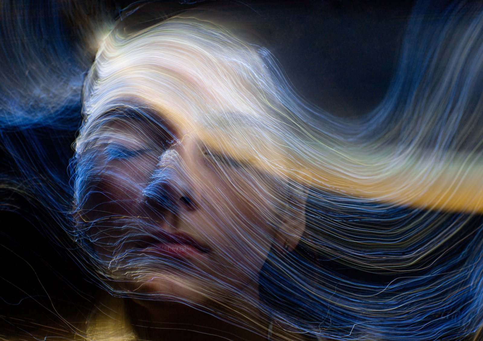 Long-exposure light trails streaming across a person's profile, the face left unresolved mid-motion
