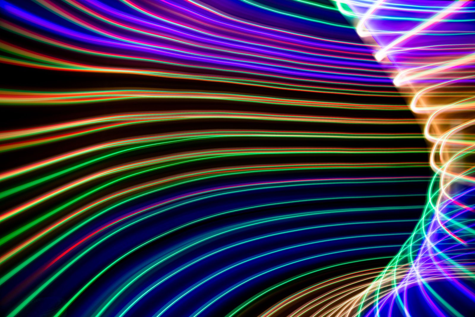 Rainbow light trails curving in a long-exposure sweep, evoking motion flowing through a system
